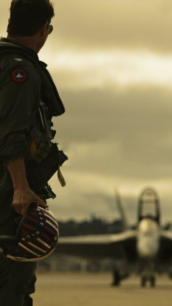 A Top Gun Maverick pilot stands holding his helmet near a fighter jet on the runway, 4K Mobile Wallpaper