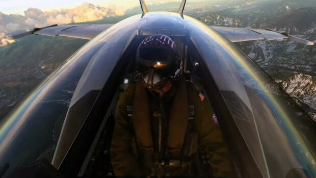 A Top Gun Maverick pilot is flying in a jet with mountains below and clouds above, HD Desktop Wallpaper