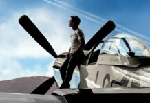 A pilot is leaning on a vintage fighter plane while looking at the sky in this Top Gun Maverick scene, HD Desktop Wallpaper