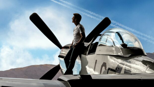 A pilot is leaning on a vintage fighter plane while looking at the sky in this Top Gun Maverick scene, HD Desktop Wallpaper