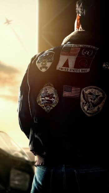 A Top Gun Maverick pilot wearing a jacket with Navy patches looks outside at a plane flying in the sky, 2K Mobile Wallpaper