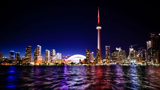 The CN Tower stands tall over Toronto with city lights reflecting in the water, 2K Desktop Wallpaper