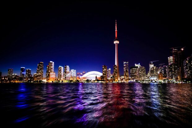The CN Tower in Canada stands tall above the illuminated city skyline reflected on the water at night