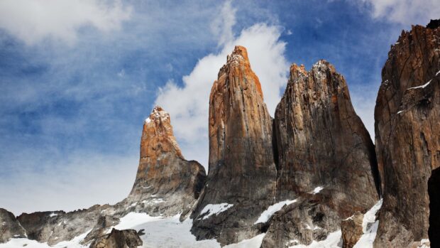 The Torres Del Paine National Park peaks rise sharply under a blue sky with scattered clouds, 4K Desktop Wallpaper