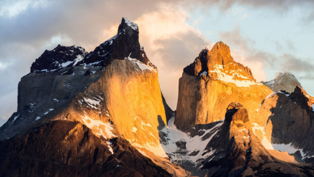 The Torres Del Paine National Park showcases towering peaks illuminated by a warm sunset glow, 4K Desktop Wallpaper
