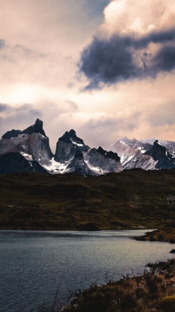The Torres Del Paine National Park shows rugged mountains with snow and a calm lake under a cloudy sky, HD Phone Wallpaper