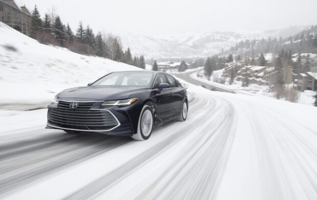 A Toyota Avalon is driving through a snow covered winding road in a mountainous area, 2K Desktop Wallpaper