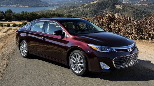 A maroon Toyota Avalon is parked on a road with mountains and trees in the background under a clear sky, HD Desktop Wallpaper