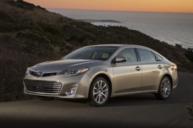 A silver Toyota Avalon is parked on a coastal road during sunset with hills in the background, 2K Desktop Wallpaper