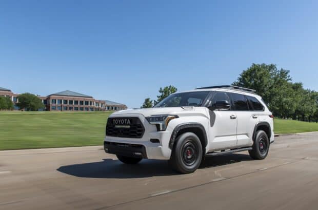 A white Toyota Sequoia is captured driving past a green lawn and buildings under a blue sky, HD Desktop Wallpaper