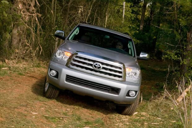 A silver Toyota Sequoia drives off road through a forested area with dense trees, 2K Desktop Wallpaper