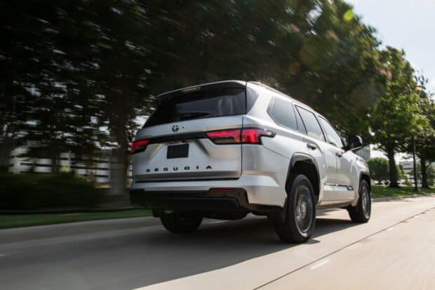 A silver Toyota Sequoia drives fast on a road surrounded by trees and buildings, HD Desktop Wallpaper