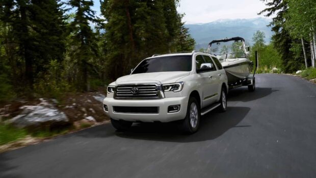 A Toyota Sequoia towing a boat on a forest road with mountains in the background, HD Desktop Wallpaper
