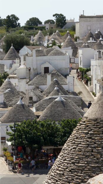 The image shows traditional Alberobello stone houses with conical roofs and people walking on the street, HD Mobile Wallpaper