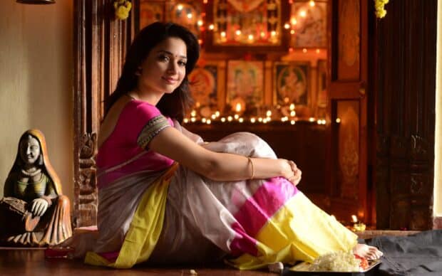 A traditional Indian woman wearing a colorful saree is sitting with a warm smile in a festive setting, 2K Desktop Wallpaper