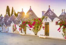 The sun shines over Alberobello with traditional trulli houses and blooming flowers, HD Desktop Wallpaper
