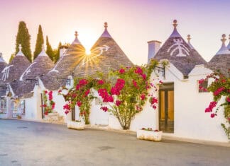 The sun shines over Alberobello with traditional trulli houses and blooming flowers, HD Desktop Wallpaper