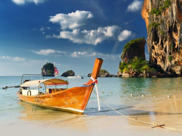 A traditional boat floats near the sandy shore with cliffs and clear skies in Phuket, HD Desktop Wallpaper