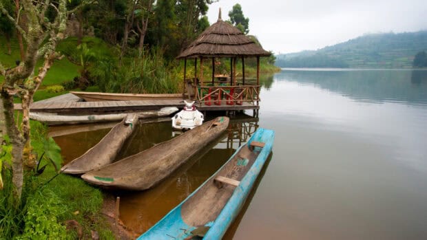 Traditional wooden boats are docked beside a calm lake surrounded by greenery in Uganda, HD Desktop Wallpaper
