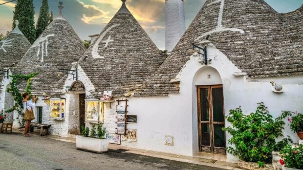 A person takes a photo of traditional stone houses with conical roofs in Alberobello, 2K Desktop Wallpaper