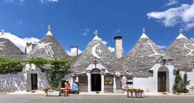 Two women are sitting outside traditional Alberobello houses on a sunny day, HD Desktop Wallpaper
