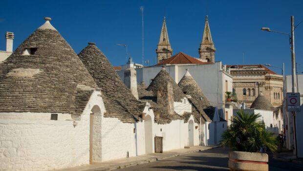 The traditional trulli houses in Alberobello are seen under a clear blue sky, 2K Desktop Wallpaper