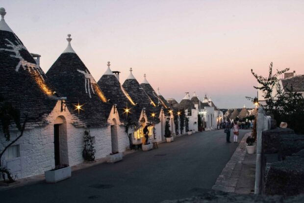 The charming street of Alberobello at dusk showcases unique trulli houses and visitors, HD Desktop Wallpaper