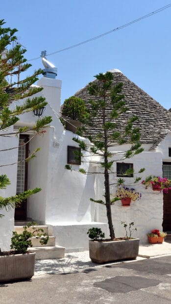 The image shows traditional white houses with conical roofs under a clear sky in the Alberobello area, HD Phone Wallpaper