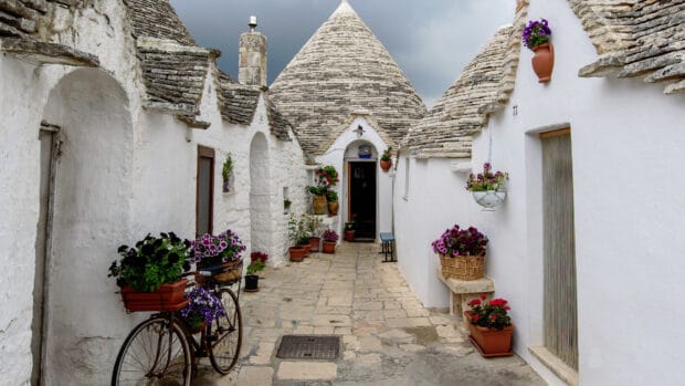 A serene street with traditional white stone houses and flowers in Alberobello, 4K Desktop Wallpaper
