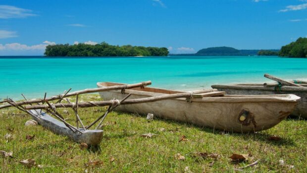 A traditional wooden boat rests on the grass by the turquoise water of Espiritu Santo Vanuatu, HD Desktop Wallpaper