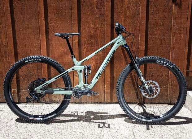 A green Transition bike is standing against a wooden wall in bright sunlight displaying its full frame, HD Desktop Wallpaper