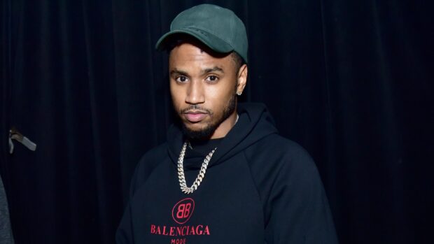 Trey Songz wears a green cap and a black hoodie with a silver chain necklace in front of a dark background, 2K Desktop Wallpaper