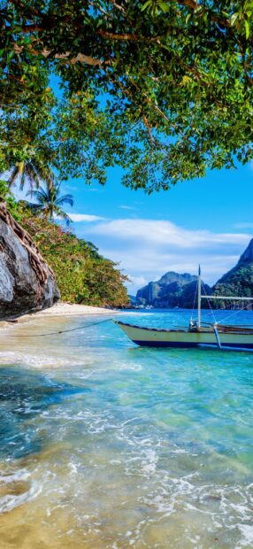 A boat on clear water near a tropical beach with lush trees in Palawan, 2K Phone Wallpaper