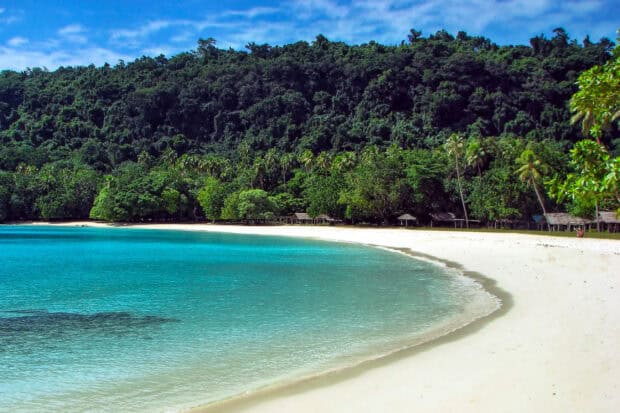 A clear blue sea and sandy shore at Espiritu Santo Vanuatu with lush green forest in the background, 2K Desktop Wallpaper
