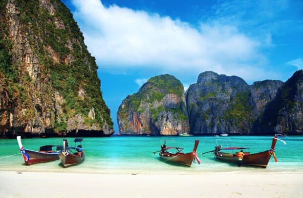 Tropical limestone cliffs rise above clear turquoise water with boats on the sandy shore in Phuket Wallpapers, 2K Desktop Wallpaper