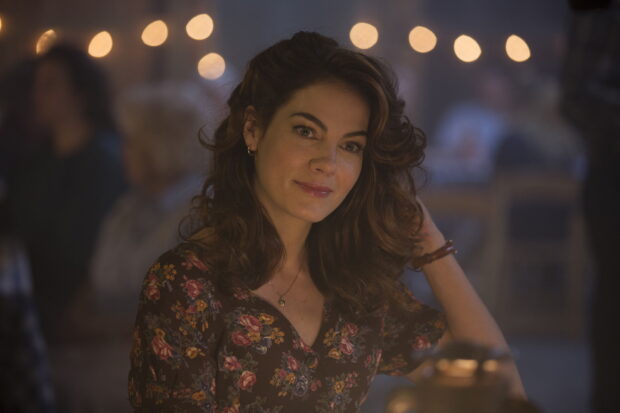 A woman with curly hair smiles softly in a dimly lit setting from True Detective Tv Series, 2K Desktop Wallpaper
