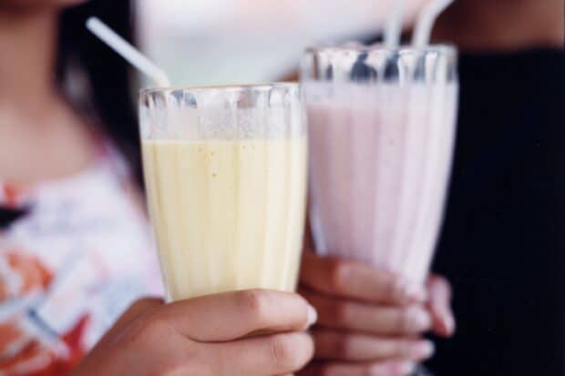 A person is holding two creamy milkshakes in glass tumblers with straws, 2K Desktop Wallpaper