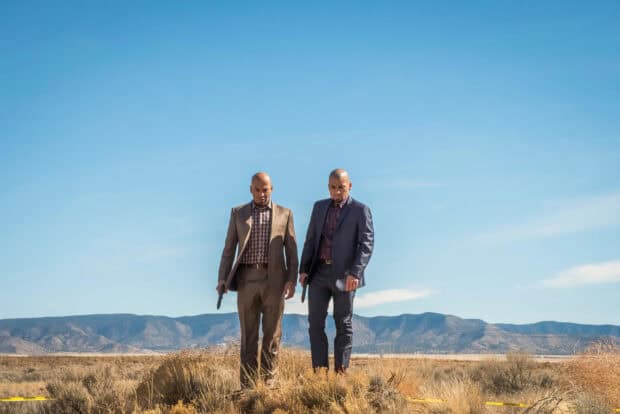 Two men holding guns walking in a dry desert area with mountains in the background, HD Desktop Wallpaper