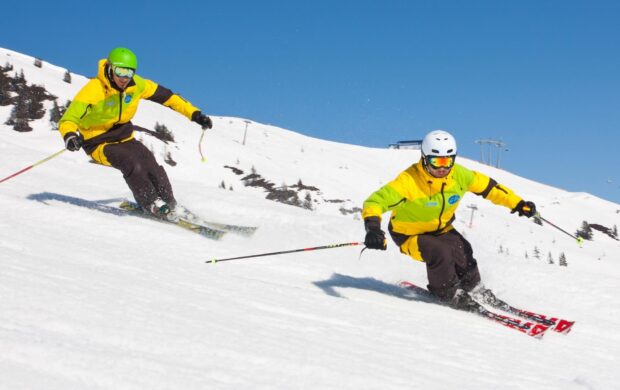 Two skiers are skiing down a snowy slope wearing bright yellow jackets under a clear blue sky, HD Desktop Wallpaper