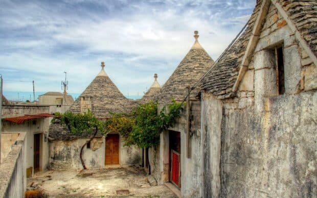 Traditional trulli houses with conical roofs in Alberobello against a cloudy sky, 2K Desktop Wallpaper