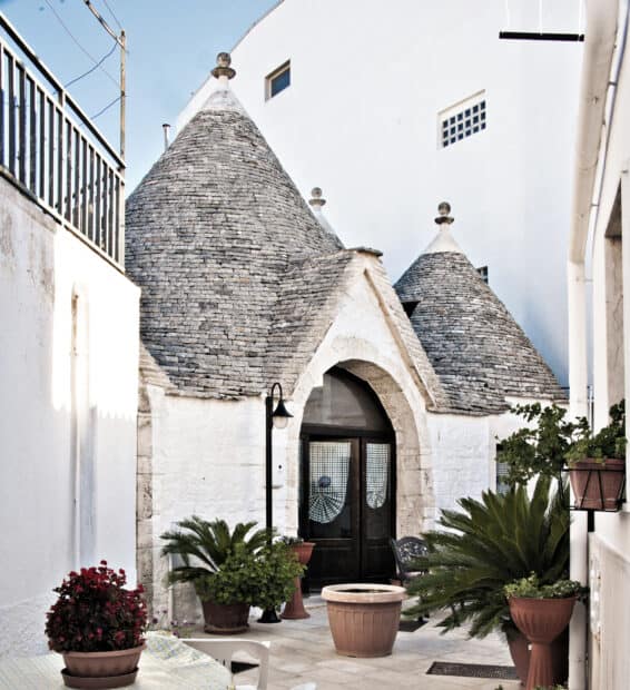 Traditional Alberobello stone houses stand with various potted plants around the entrance, HD Desktop Wallpaper
