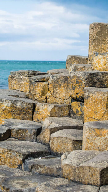 The Giants Causeway features distinct hexagonal basalt columns near the ocean under a cloudy sky, HD Mobile Wallpaper