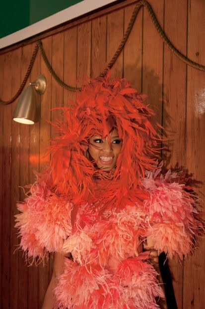 A model wearing a vibrant feathered dress with shades of orange and pink, 2K Desktop Wallpaper