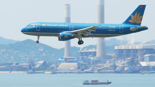 A Vietnam Airlines airplane flying over water near an industrial area, 2K Desktop Wallpaper