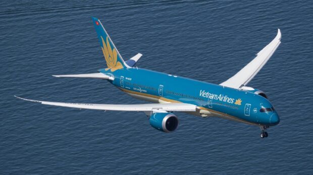 A Vietnam Airlines plane is captured flying above the sea with its distinctive blue and gold livery, 2K Desktop Wallpaper