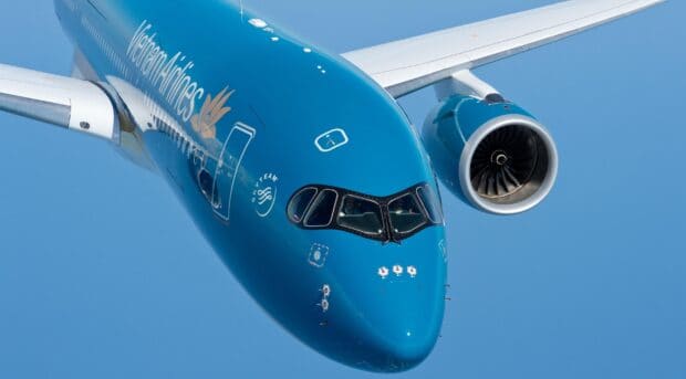 A Vietnam Airlines is flying in a clear blue sky showing the front and engine, 2K Desktop Wallpaper