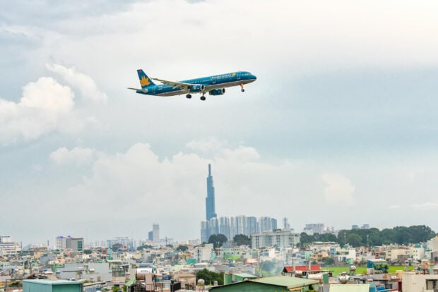 A Vietnam Airlines airplane is flying over a cityscape with a tall skyscraper in the background, HD Desktop Wallpaper