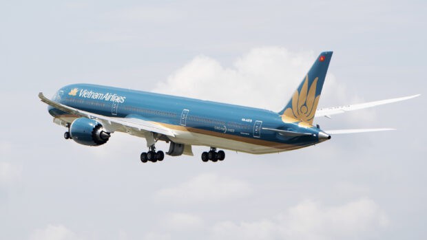 A Vietnam Airlines airplane is flying with its landing gear partially retracted in a clear sky, 2K Desktop Wallpaper