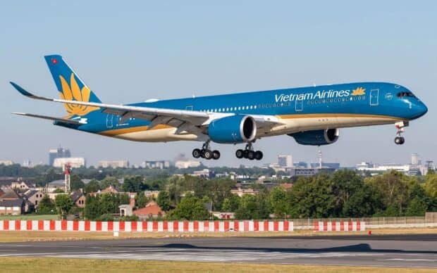 A Vietnam Airlines airplane is captured flying over an airport runway with clear skies, HD Desktop Wallpaper