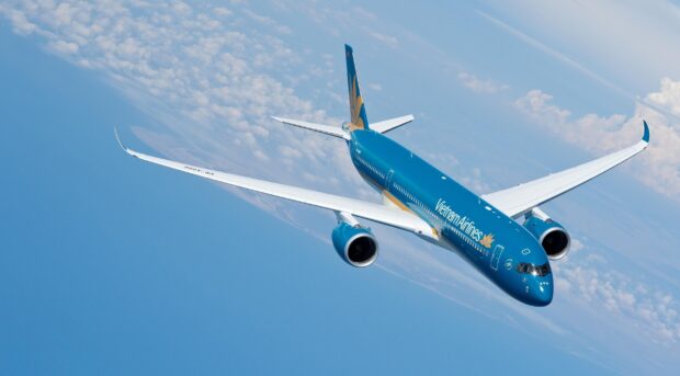 A Vietnam Airlines jet is captured flying above the clouds with clear blue skies, 2K Desktop Wallpaper